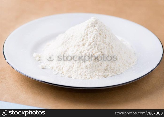 Heap of wheat flour on white plate, selective focus