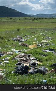 Heaps of garbage in the nature. Green grass and mountains on background. Ecology and waste collection concept.