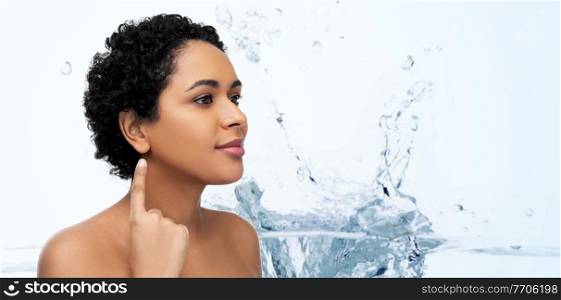 hearing, health and beauty concept - portrait of happy smiling young african american woman with bare shoulders showing her ear over water splash on blue background. african american woman showing her ear