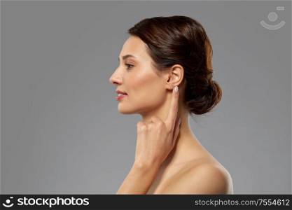hearing, people and beauty concept - beautiful young woman pointing finger to her ear over grey background. beautiful young woman pointing finger to her ear