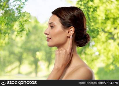 hearing, people and beauty concept - beautiful young woman pointing finger to her ear over green natural background. beautiful young woman pointing finger to her ear