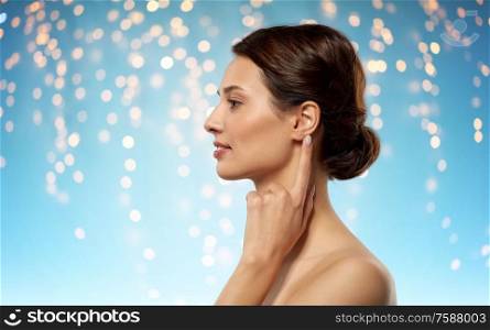 hearing, people and beauty concept - beautiful young woman pointing finger to her ear over holidays lights on blue background. beautiful young woman pointing finger to her ear