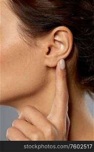 hearing, people and beauty concept - close up of young woman pointing finger to her ear over grey background. close up of young woman pointing finger to her ear