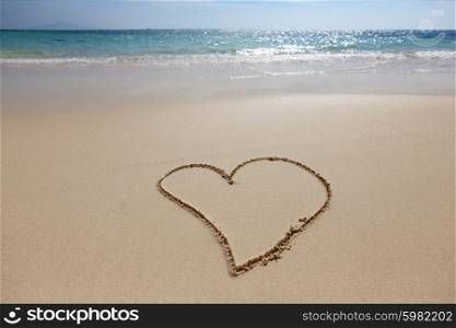 Heart drawing in the sand on the beach, blue waves on background