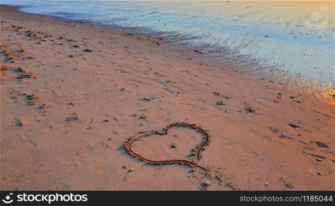heart drawn in the sand on a beach at sunset