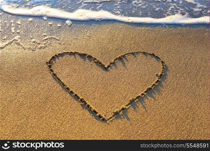 Heart drawn on the beach sand with sea foam and wave