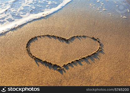 Heart drawn on the beach sand with sea foam and wave