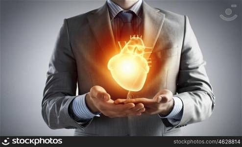 Heart health care. Close up of businessman holding digital glowing heart in palm
