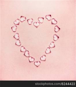 Heart made from glass hearts on pale pink background, top view