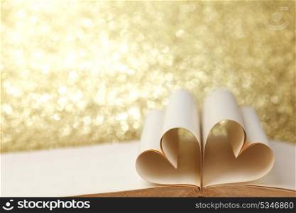 Heart made of blank pages inside a book on glitter background