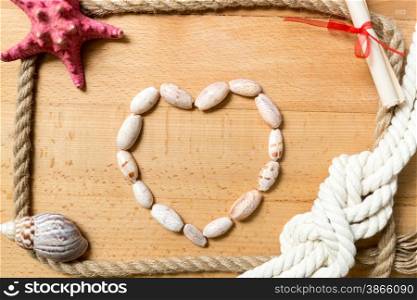 Heart made of seashells with border of ropes and knots on wooden background