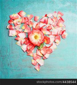 Heart made ??out of pink pale rose petals on blue turquoise background, top view. Festive greeting card