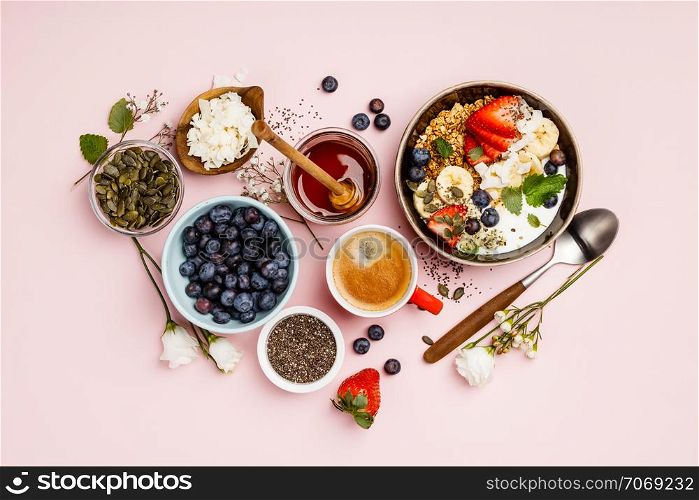 Heart made with Healthy breakfast set. Oat granola with fresh berries, banana, yogurt, maple syrup, seeds and mint leaves with cup of coffee on pink background, flat lay, top view