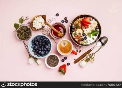 Heart made with Healthy breakfast set. Oat granola with fresh berries, banana, yogurt, maple syrup, seeds and mint leaves with cup of coffee on pink background, flat lay, top view