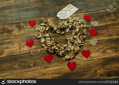 Heart maked with dry petals on a wooden background