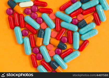 Heart medicine. Pills arranged in heart shape on an orange background