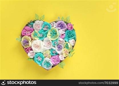 heart of artificial flowers handmade on a yellow paper background. Copy space.
