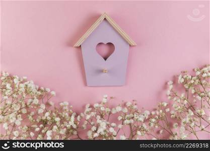 heart shape bird house with decorated gypsophila flowers pink background
