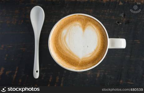 Heart Shape Froth Milk Latte Art in White Coffee Cup and Spoon on Black Wood Table. Heart shape froth milk Latte art hot beverage for coffee lover