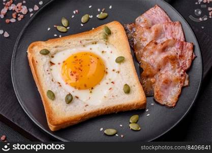 Heart shaped fried egg in bread toast with sesame seeds, flax seeds and pumpkin seeds on a black plate on a dark concrete background