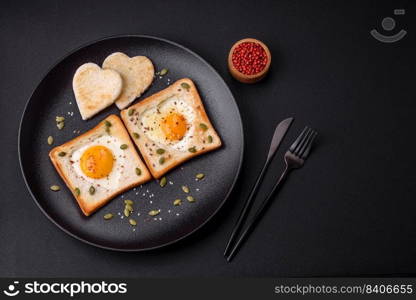 Heart shaped fried egg in bread toast with sesame seeds, flax seeds and pumpkin seeds on a black plate on a dark concrete background