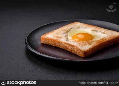Heart shaped fried egg in bread toast with sesame seeds, flax seeds and pumpkin seeds on a black plate on a dark concrete background
