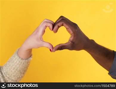 Heart shaped hands black hand and white hand, interracial, on yellow background