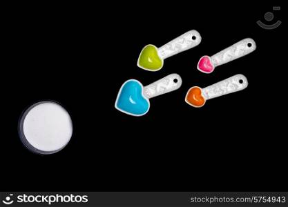 Heart shaped measuring spoons of diffferent sizes and colors facing the direction of a round bowl of sugar bringing together the ideas of love, conception and food, or sweet stuff. All on a black isolated background.