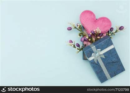 Heart-shaped pillow and mini flower in gift box on blue background, valentine concept.