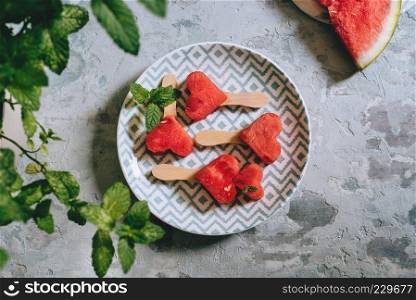 Heart-shaped slices of watermelon, in a dish with a geometric design, over a rustic blue texture. Heart-shaped slices of watermelon