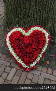 Heart shaped sympathy floral arrangement near a tree