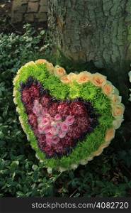 Heart shaped sympathy flower arrangement in green, pink and yellow