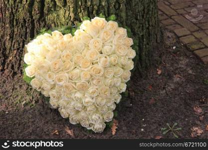 Heart shaped sympathy flower arrangement with white roses near a tree