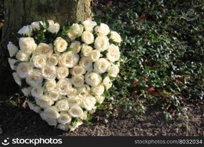 Heart shaped sympathy flower arrangement with white roses near a tree