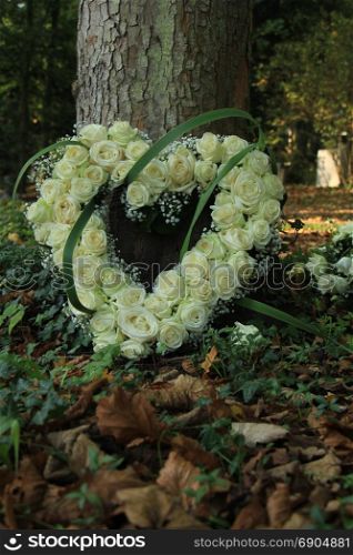 Heart shaped sympathy flowers made from white roses near a tree at a cemetery