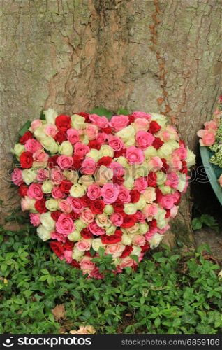 Heart shaped sympathy flowers near a tree at a cemetery