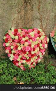 Heart shaped sympathy flowers near a tree at a cemetery