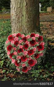Heart shaped sympathy flowers or funeral flowers near a tree, pink roses and gerbers and Eucalyptus