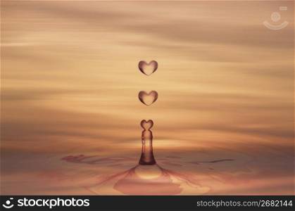 Heart shaped water droplets, falling into a sunset coloured water