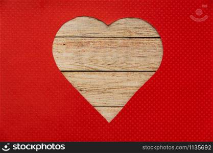 Heart shaped wooden hole torn through paper, isolated on red background. Top view with space for your greetings.