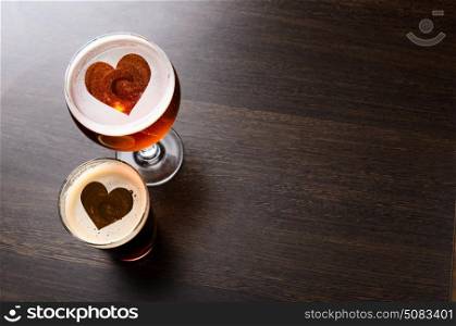 Heart silhouettes in two glasses of fresh beer on pub table, view from above