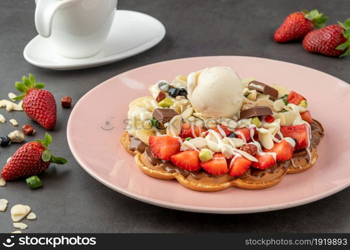 Heart waffle with banana and strawberry with gummy candy and ice cream on it.