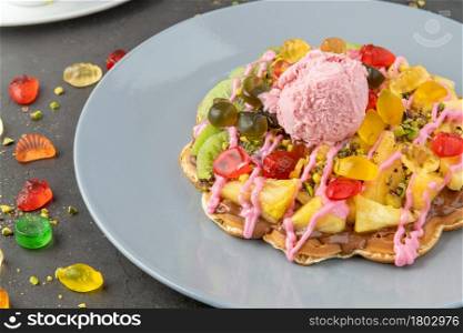 Heart waffle with kiwi and pineapple with gummy candy and ice cream on it.