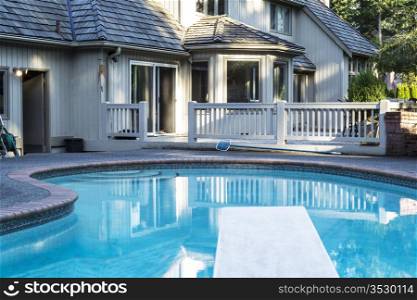 Heated outdoor swimming pool with large home in background with green trees