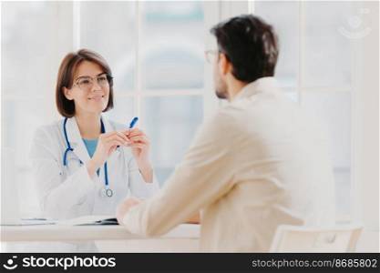 Heath care and medical consultancy concept. Skilled therapist in white uniform talks with patient, writes down in medical history, listens attentively all symptoms, tries to prevent serious disease
