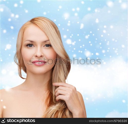heath, people, haircare and beauty concept - beautiful young woman with bare shoulders touching her hair over blue sky, snow and clouds background