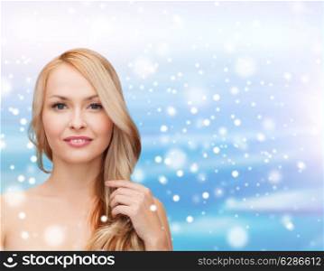 heath, people, haircare and beauty concept - beautiful young woman with bare shoulders touching her hair over blue sky, snow and clouds background