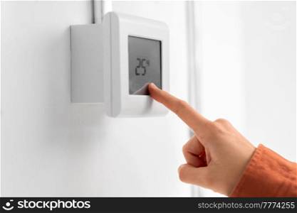 heating, energy and power consumption concept - close up of hand setting room temperature on thermostat at home. hand setting room temperature on sensor at home