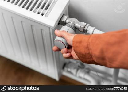 heating, energy crisis and consumption concept - close up of hand turning radiator toggle switch at home. close up of hand turning radiator toggle at home