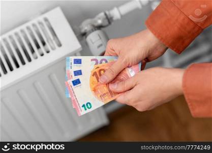 heating, energy crisis and consumption concept - close up of hands with money on radiator at home. close up of hands with money on radiator at home